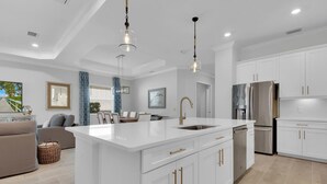 A modern kitchen with white cabinetry, a central island, stainless steel appliances, and pendant lighting. - Gated Resort Community Pool Home (Estero)