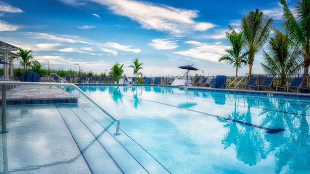 A clear blue pool with lounge chairs and umbrellas, surrounded by palm trees. - Gated Resort Community Pool Home (Estero)