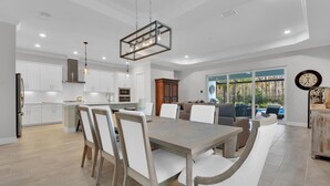 A modern kitchen with white cabinetry, a dining area with a wooden table and chairs, and a view of a pool through large windows. - Gated Resort Community Pool Home (Estero)