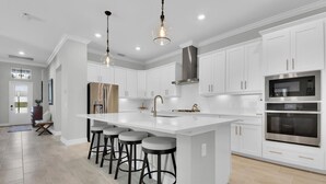 A modern kitchen with white cabinetry, a large island with bar stools, stainless steel appliances, and pendant lighting. - Gated Resort Community Pool Home (Estero)