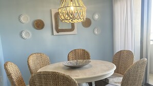 Ein Essbereich mit einem runden Tisch, sechs Korbstühlen, einer gewebten Pendelleuchte und dekorativen Tellern an der Wand.
