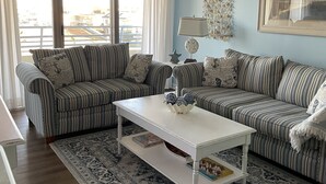 Ein Wohnzimmer mit gestreiften Sofas, einem weißen Couchtisch, einem gemusterten Teppich und einem großen Fenster mit Vorhängen.
