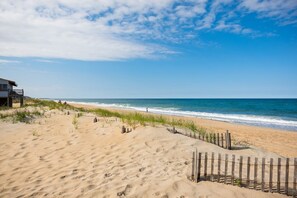 A sandy beach with a wooden fence, a building with a balcony, and the ocean in the background. - Beachside-Ocean views & Great beach access (Kitty Hawk)