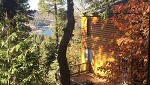 A log cabin with a deck overlooking a forested area and a body of water. - Peaceful Cozy Cabin Amongst the Trees with View of Lake Arrowhead (Lake Arrowhead)
