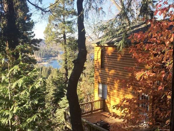 A log cabin with a deck overlooking a forested area and a body of water.