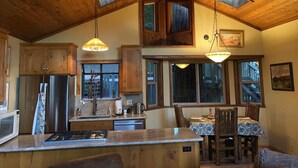 A kitchen with wooden beams, a stainless steel refrigerator, a sink, and a dining area with a table and chairs. - Peaceful Cozy Cabin Amongst the Trees with View of Lake Arrowhead (Lake Arrowhead)