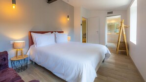Quarto moderno com uma cama grande, luminárias laterais, uma escada de madeira e vista para um banheiro.