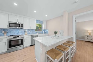 A modern kitchen with white cabinets, stainless steel appliances, and a large island with bar stools.