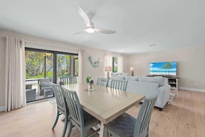 A spacious living room with a large dining table, a white sofa, and a television.