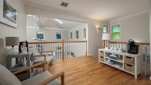 Een ruime woonkamer met houten vloer, een witte leuning en een eethoek met een bijzettafeltje en stoelen.