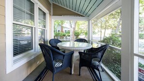 Een overdekt terras met een glazen tafel en vier rieten stoelen.
