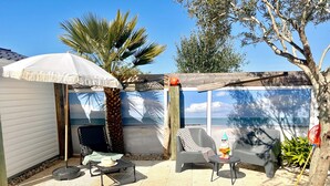 Eine Terrasse mit zwei Stühlen, einem kleinen Tisch, einem weißen Sonnenschirm und einer Ziergnom.