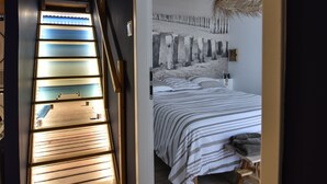 Ein Schlafzimmer mit einem Bett, einem Nachttisch, einem Wandbild und einer Treppe mit beleuchteten Stufen.