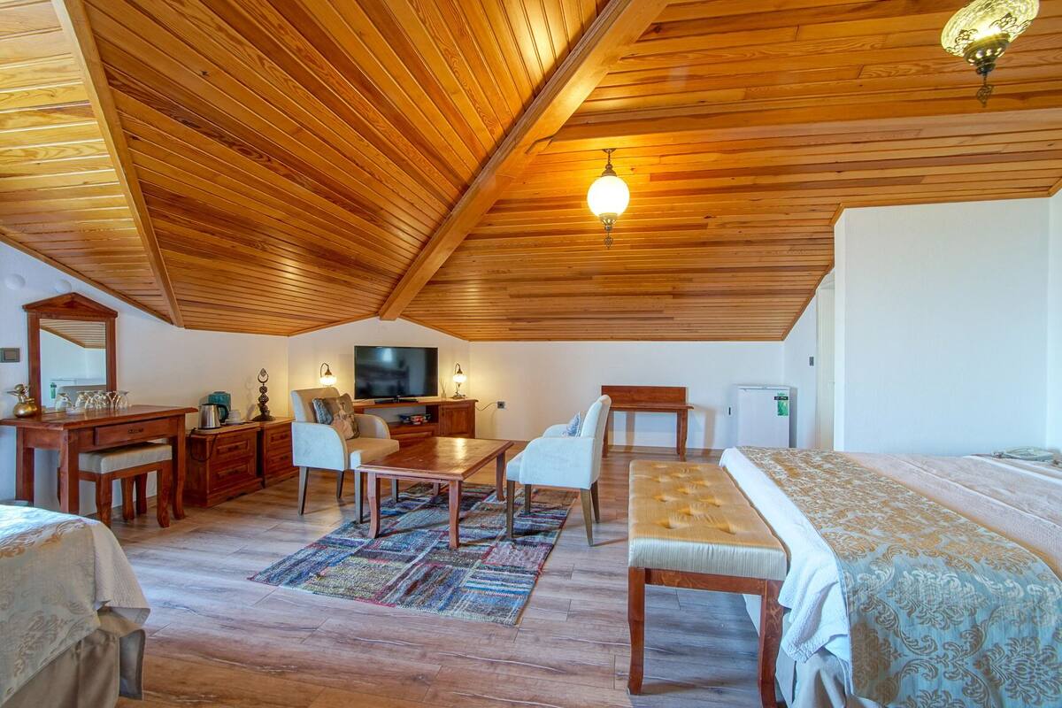 A cozy room with wooden ceiling beams, a television, a dining table, and a bed.