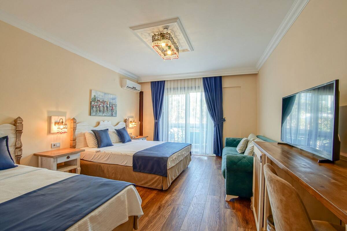 A hotel room with two beds, a TV, a desk, and a window with curtains.