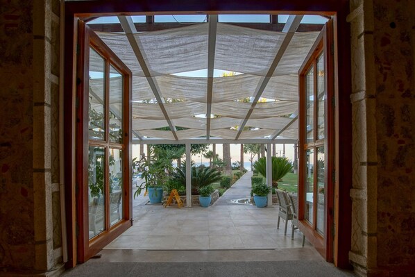 A covered outdoor area with a glass door leading to a patio with potted plants and a view of the outdoors. - My Marina Select Hotel (Datça)