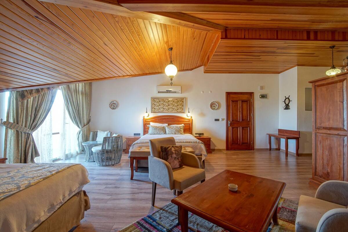 A cozy room with a large bed, two smaller beds, a wooden ceiling, a dining table, and a bench.