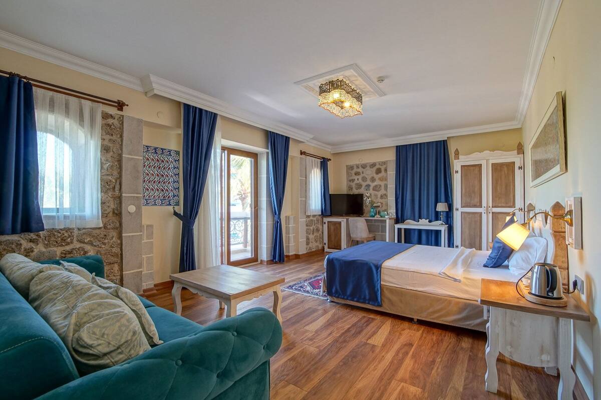 A hotel room with a bed, a desk, a chair, a sofa, a television, and a window with curtains.