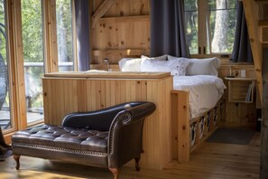 Ein Schlafzimmer einer Holzhütte mit einem Bett, einer Bank und einem Fenster mit Vorhängen.