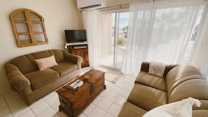 A living room with a sofa, a wooden coffee table, a TV, and a sliding glass door leading to an outdoor area. - Beachfront Retreat with Convenient Access to Shops, Dining, and More (San José del Cabo)