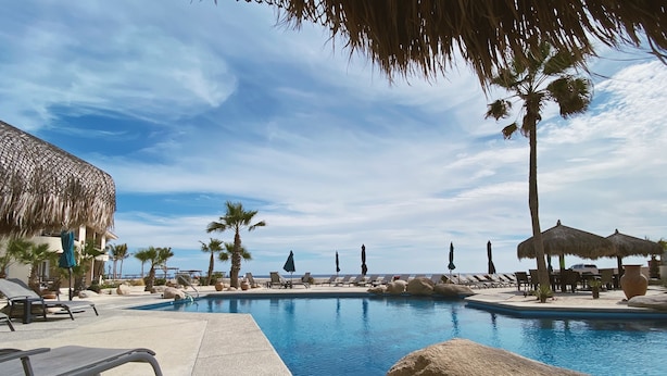 A pool area with lounge chairs, umbrellas, and palm trees. - Beachfront Retreat with Convenient Access to Shops, Dining, and More (San José del Cabo)