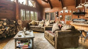L’intérieur chaleureux d’un chalet avec un plafond en bois, un ensemble de canapés, une table à manger et un coin cuisine.