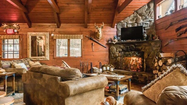 L’intérieur d’un chalet rustique, avec une cheminée en pierre, des murs en bois et une tête de cerf accrochée au mur.