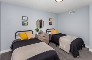 Ein Schlafzimmer mit zwei Betten, einem Schminktisch, einem Spiegel und Wandbildern.
