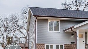 A two-story house with a garage, a front porch, and a brick foundation. - A Charming Home Minutes to Downtown, Zoo, & Airport with Hidden Reading Nook! (Des Moines)