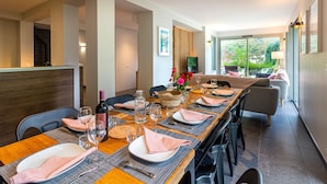 A dining area with a long table set for six, a wine bottle, and a flower centerpiece.