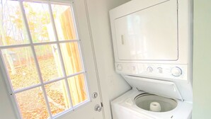 A laundry room with a front-loading washer and dryer, a white door, and a window with a view of trees. - Renovated cabin / beach access / 1+ acre of woods (South Haven)