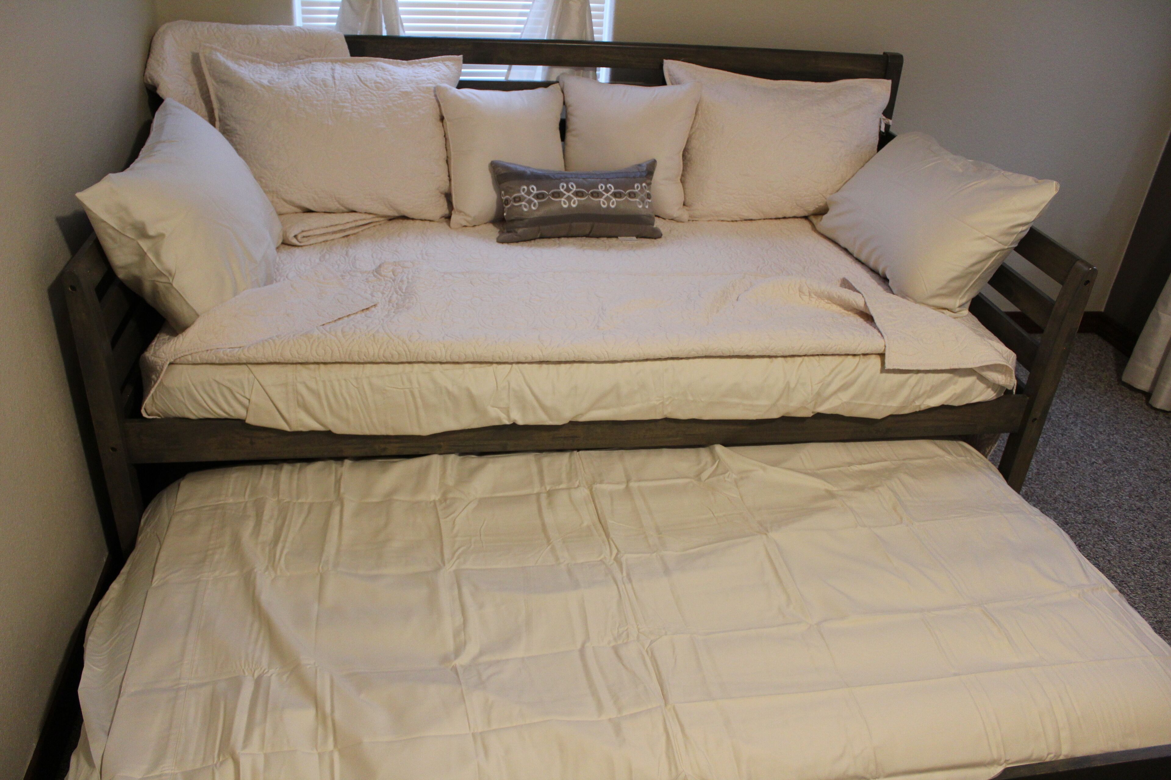 Una cama con estructura de madera, ropa de cama blanca y un cojín decorativo.