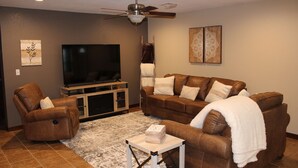 A living room with a brown leather sofa, a brown leather armchair, a white coffee table, a flat-screen TV, and a ceiling fan. - Quiet and Comfortable!  5 minutes away from parks/hospitals (Joplin)