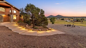 A modern house with a stone pathway leading to a seating area, surrounded by a landscaped garden and a view of a mountain at dusk. - 🌅 Sunset Ranch 🌅 Views Views Views with Private Indoor Pickelball Court (Flagstaff)