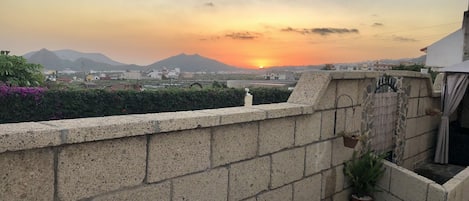 A rooftop terrace with a view of the sunset, a stone wall, and a small garden area with a potted plant.