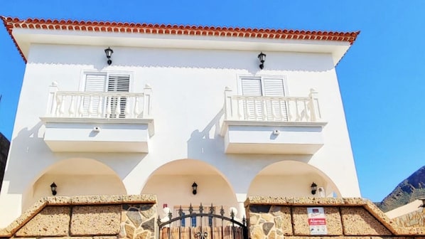 Un bâtiment blanc doté de deux balcons, d’un portail en pierre et surplombant un ciel d’un bleu limpide.