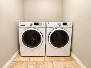 A pair of front-loading washing machines in a corner with a tiled floor.