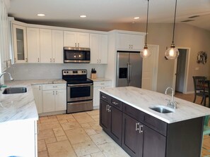 A modern kitchen with white cabinets, stainless steel appliances, a marble countertop, and pendant lighting.