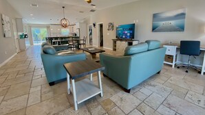 A spacious living room with a sofa set, a coffee table, and a TV. There is a dining area in the background with a chandelier. - Mystical - Relaxing Heated Pool and Stylish Comfortable Home, Pet Friendly! (St. Augustine)