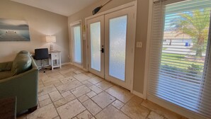A spacious room with a large sliding glass door leading to a balcony, a comfortable seating area with a sofa and a desk, and a painting on the wall. - Mystical - Relaxing Heated Pool and Stylish Comfortable Home, Pet Friendly! (St. Augustine)