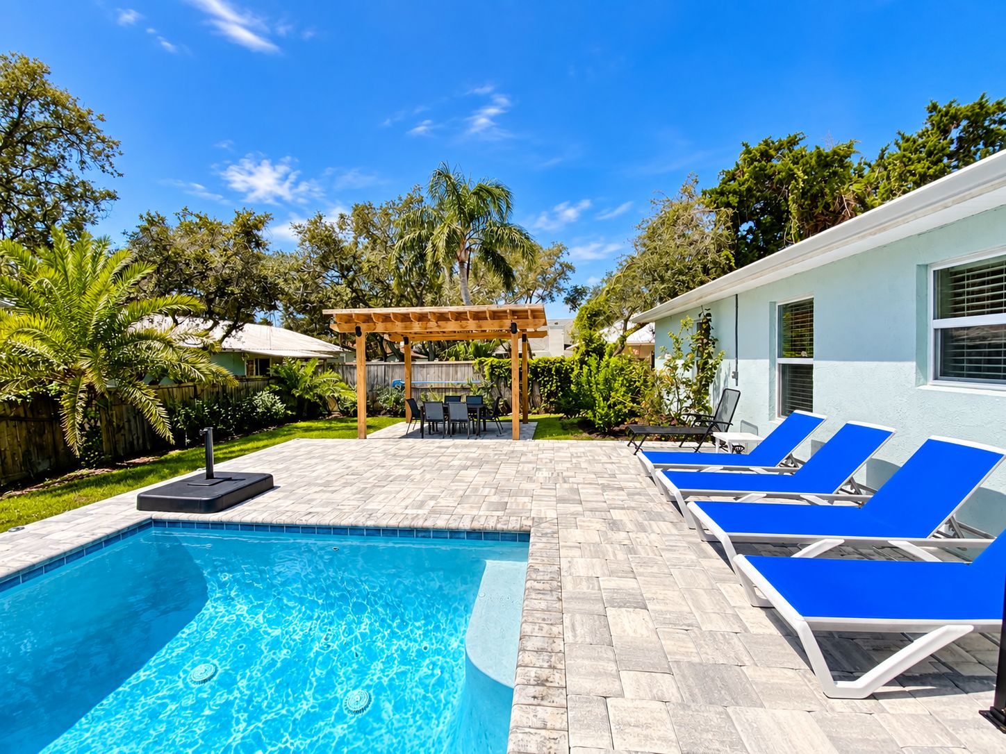 A swimming pool with lounge chairs and a pergola in a backyard.
