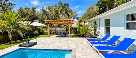 A swimming pool with lounge chairs and a pergola in a backyard.