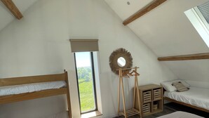 Ein Schlafzimmer mit zwei Etagenbetten, einem Fenster mit Blick, einem Holzboden und einem runden Spiegel.