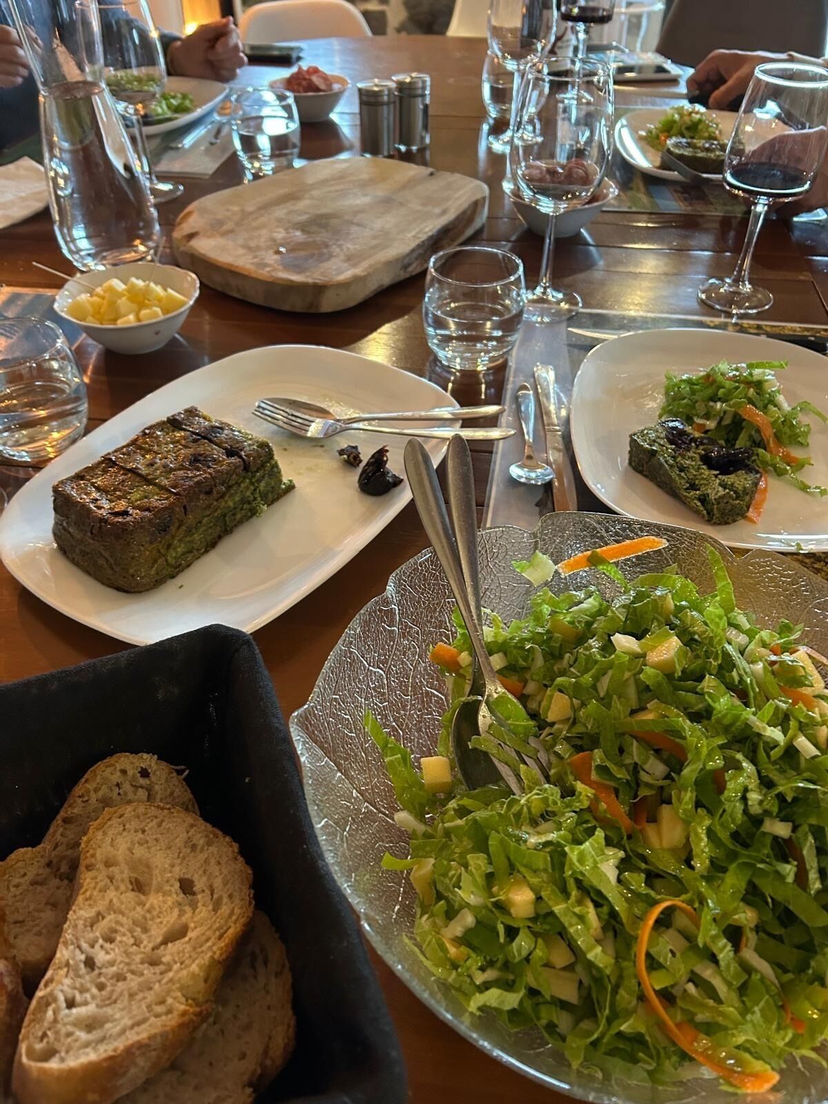 A dining table with plates of food, including a green dish, a salad, and bread.