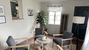 Un salon avec quatre fauteuils gris à revêtement en tissu, une table basse ronde, une plante en pot et une grande fenêtre avec des rideaux.