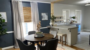 Un coin repas avec une table ronde, quatre chaises, un tapis et une cuisine en arrière-plan.