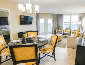 A hotel room with a dining area, a living area, a balcony with curtains, and a TV mounted on the wall. - Luxury Condo Near Disney (Kissimmee)