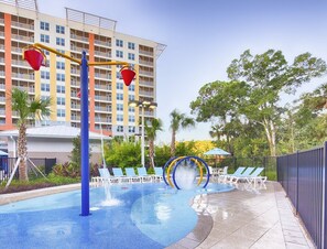 A swimming pool with a water feature, surrounded by lounge chairs and a fence. - Luxury Condo Near Disney (Kissimmee)