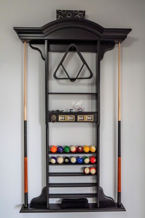A pool table with a rack holding balls and cue sticks.