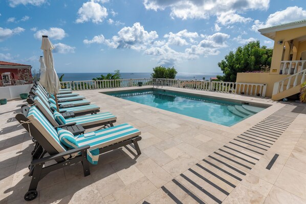 A pool area with lounge chairs and a view of the sea.